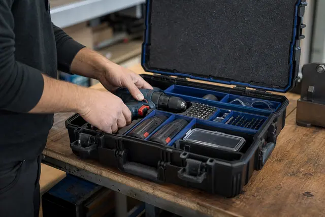 Coffret rigide compartimenté protégeant perceuse, batteries, forets et embouts sur un établi.