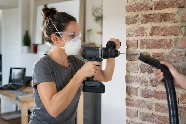Bricoleuse équipée perçant un mur en brique avec une perceuse sans fil.