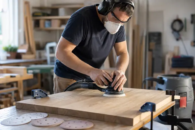 Bricoleur ponçant un plateau en chêne avec une ponceuse excentrique aspirée.