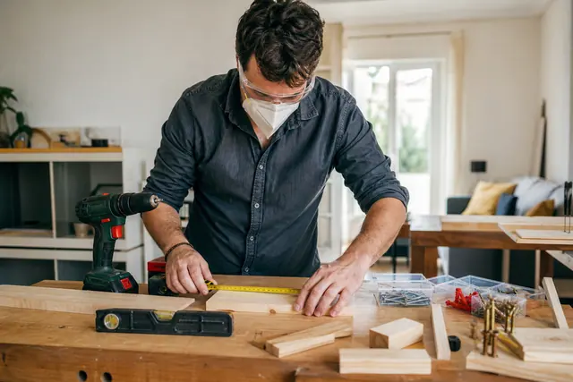 Débutant équipé préparant une planche de bois sur un établi domestique.