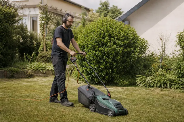 Jardinier équipé poussant une tondeuse électrique sur une pelouse sèche et dégagée.
