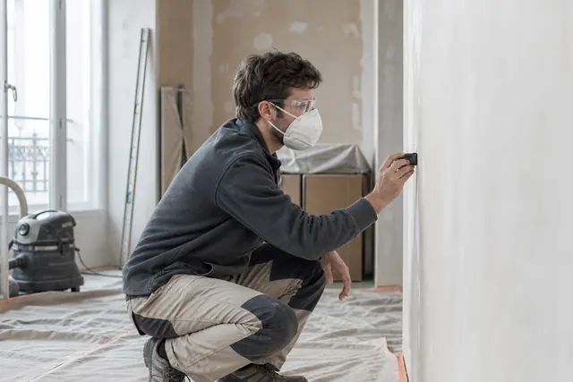 Bricoleur mesurant un mur préparé dans une pièce protégée avant rénovation.