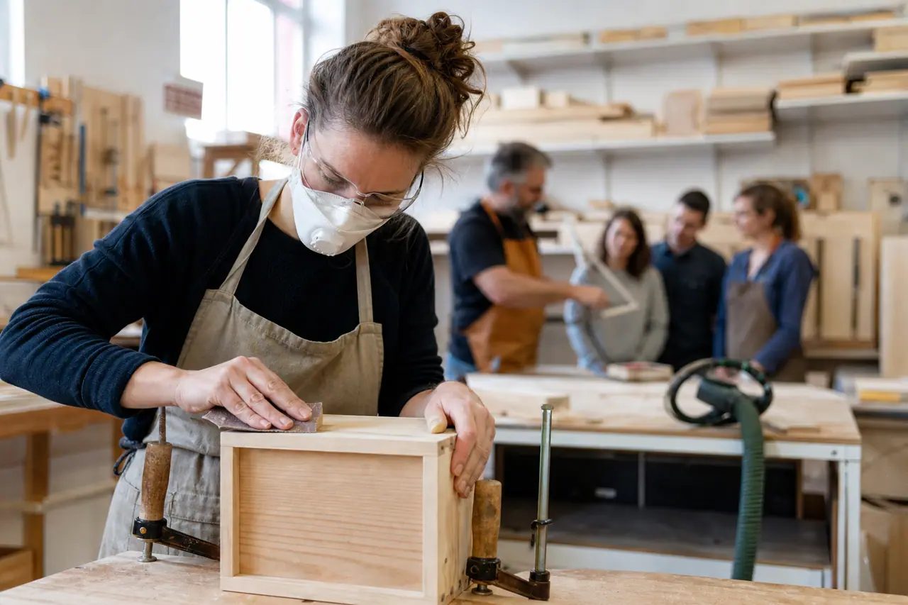 Débutante ponçant une petite caisse en bois dans un atelier encadré.