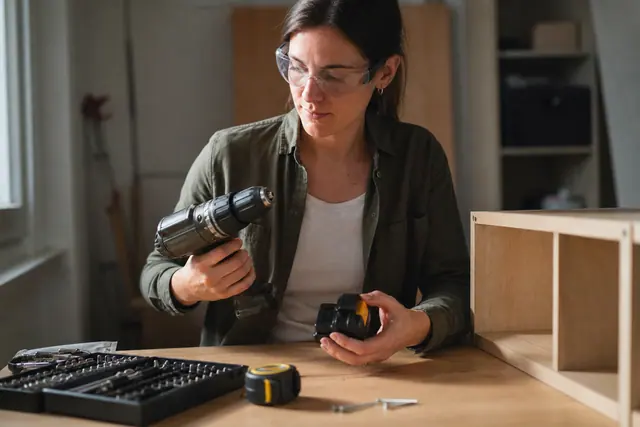 Bricoleuse portant des lunettes préparant une perceuse sur un établi domestique lumineux