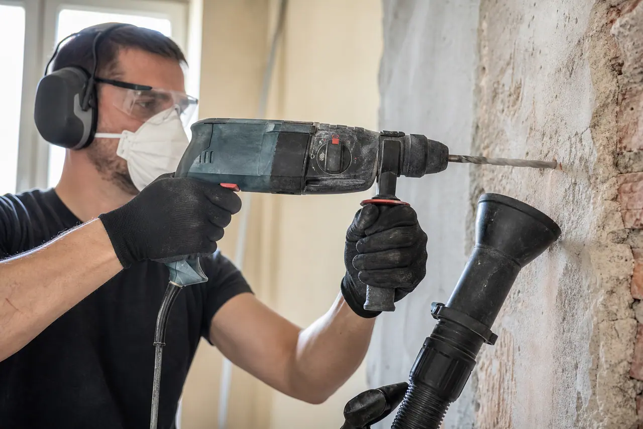 Bricoleur équipé perçant un mur de brique avec une perceuse filaire.