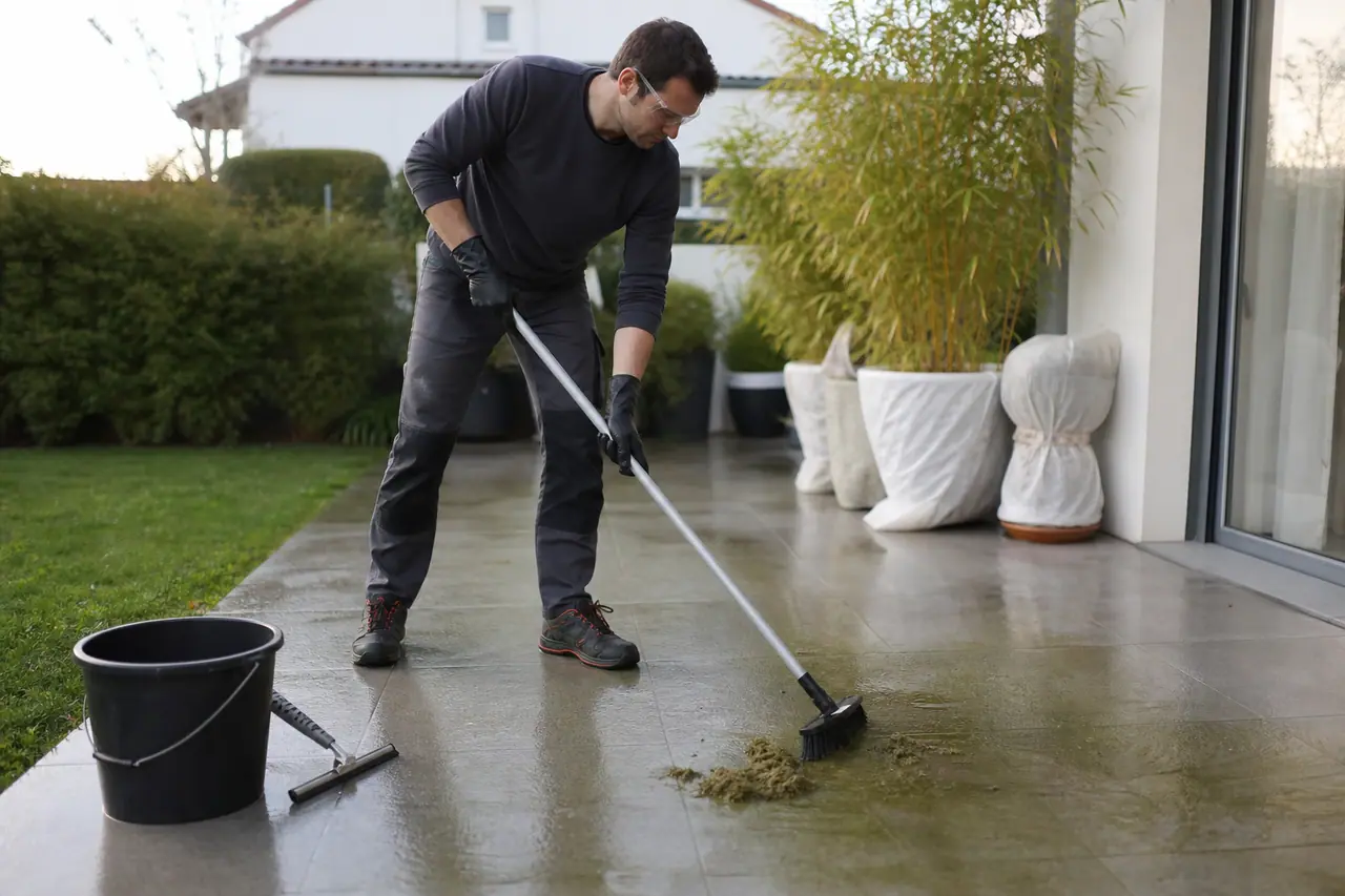 Propriétaire brossant une terrasse en dalles pour retirer la mousse humide.