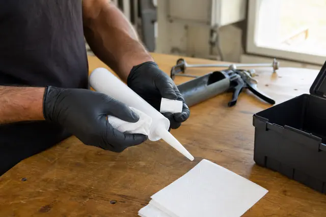 Bricoleur nettoyant et bouchant une cartouche de mastic après usage.