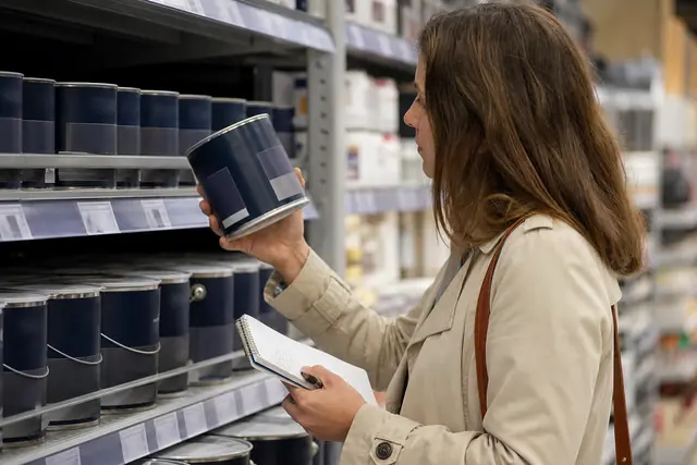 Cliente compare deux pots de peinture et leurs étiquettes de prix en magasin.