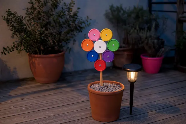 Rosace en couvercles colorés éclairée par une lampe solaire sur une terrasse.
