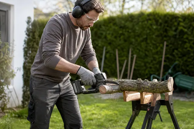 Jardinier équipé coupant une petite branche sur chevalet avec mini-tronçonneuse sans fil.
