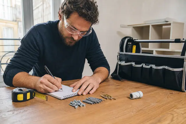 Particulier préparant une liste de bricolage avec mètre, vis et chevilles.