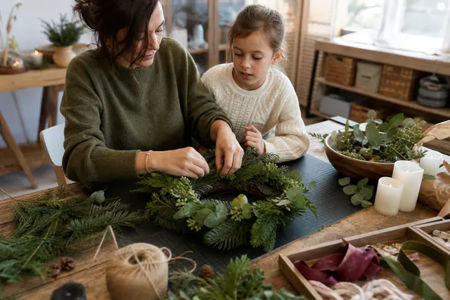 Adulte et enfant fabriquant une couronne végétale sur une table protégée.