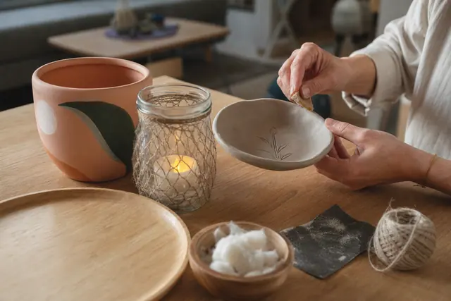 Atelier domestique avec coupelle en argile, cache-pot peint et plateau en bois.