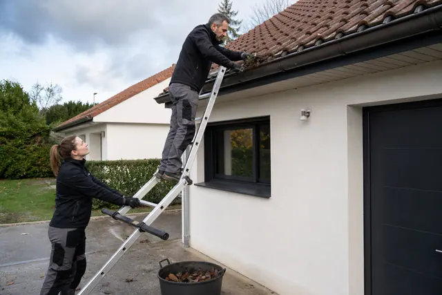 Propriétaire nettoyant une gouttière basse avec une échelle stabilisée et un seau.