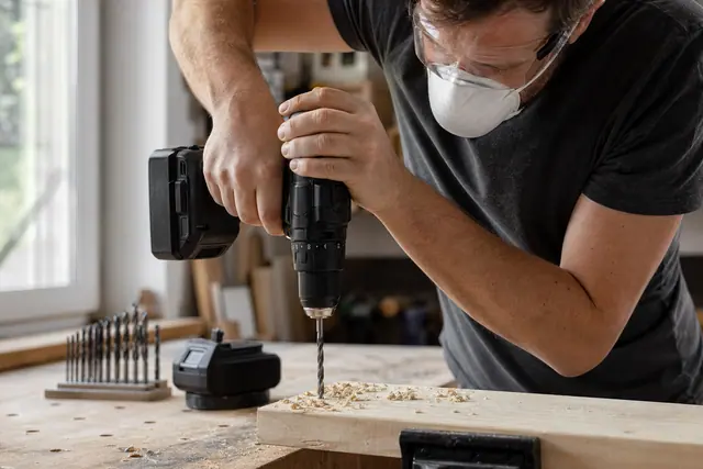 Bricoleur équipé perçant une planche sur établi avec une perceuse-visseuse compacte.