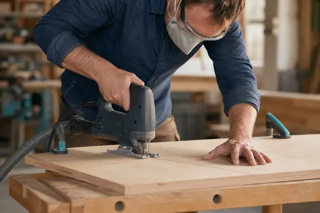 Bricoleur équipé découpant une planche fixée avec une scie sauteuse.