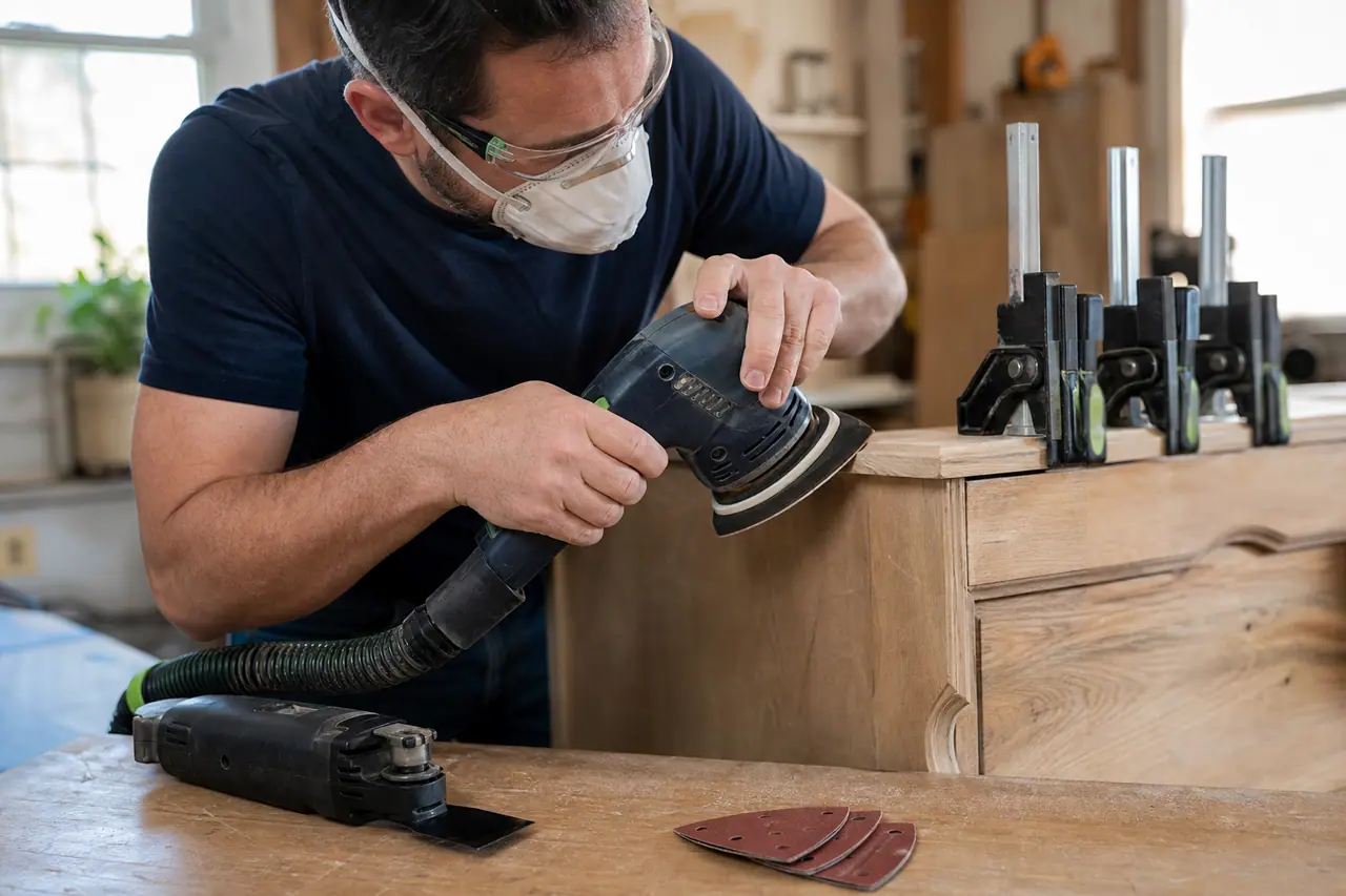 Bricoleur ponçant le chant d’une commode avec une ponceuse multifonction.