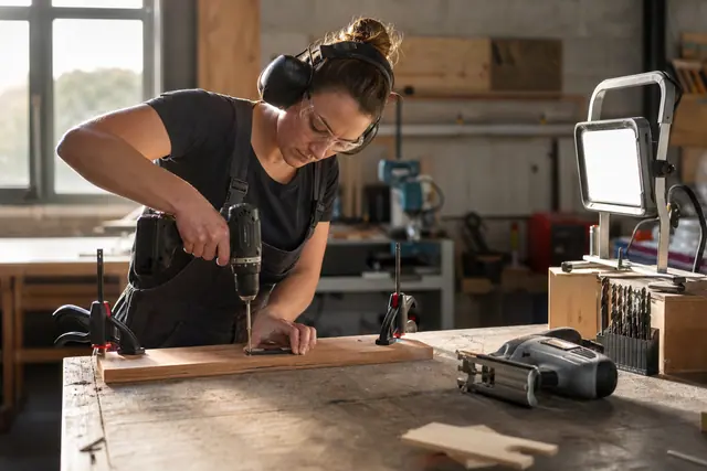 Bricoleuse équipée utilisant une perceuse sans fil sur une planche fixée à l’établi.