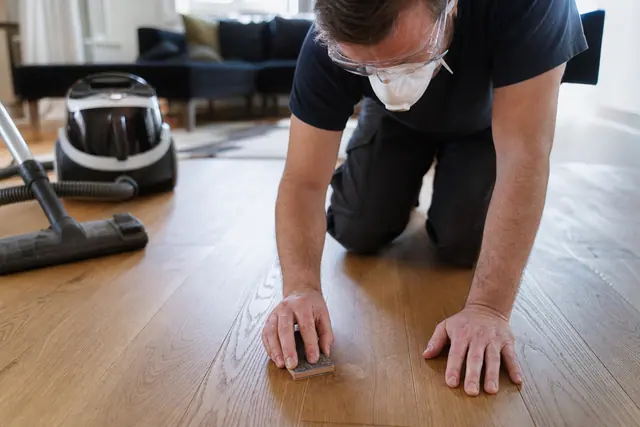 Bricoleur protégé retouchant une rayure sur un parquet en chêne mat.