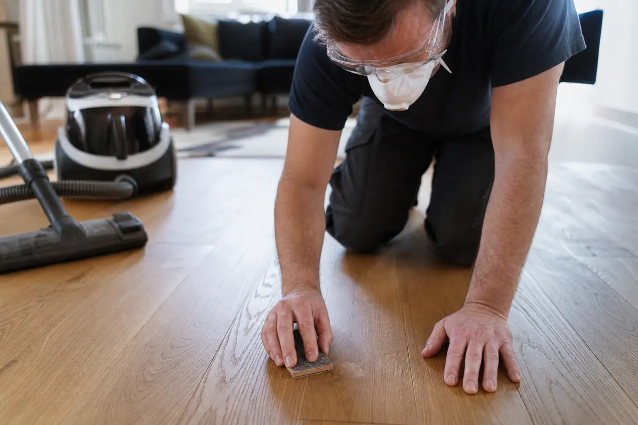 Bricoleur protégé retouchant une rayure sur un parquet en chêne mat.