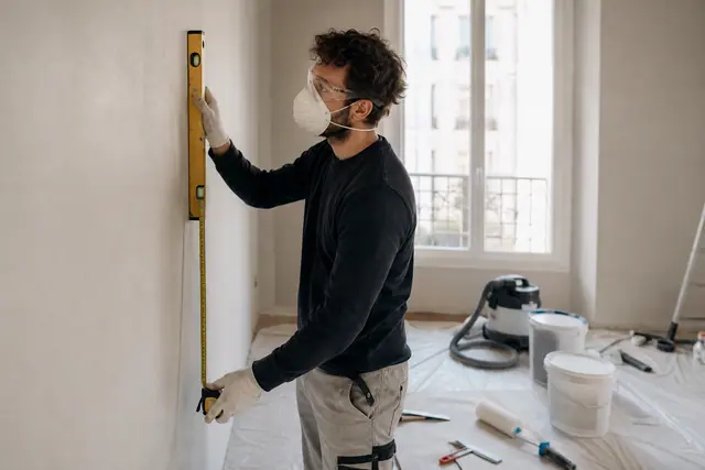 Bricoleur protégé mesurant un mur préparé dans une pièce en rénovation.