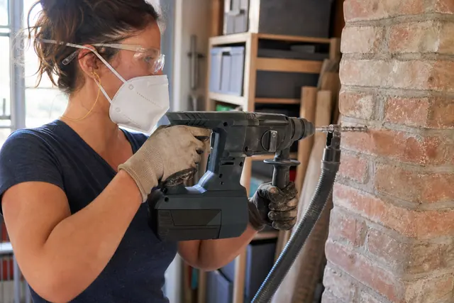 Bricoleuse équipée perçant un mur de brique avec une perceuse sans fil