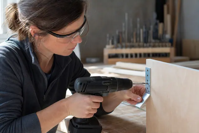 Bricoleuse vissant une équerre de meuble avec une visseuse sans fil compacte.