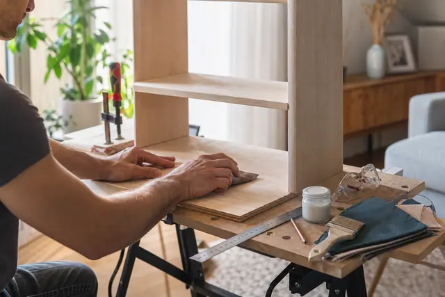 Adulte ponçant une petite étagère en bois sur un établi intérieur lumineux.