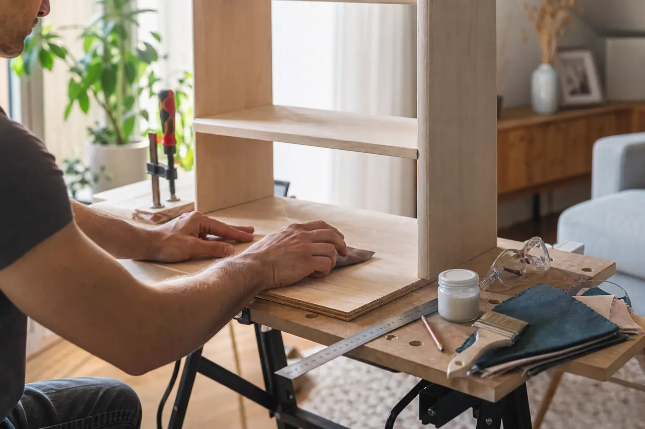Adulte ponçant une petite étagère en bois sur un établi intérieur lumineux.