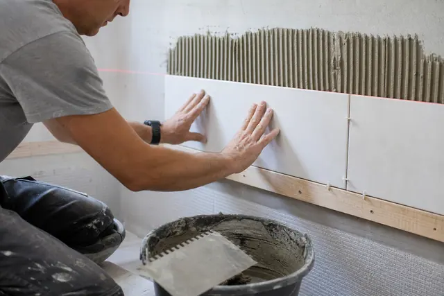 Carreleur posant de la faïence sur un mur de salle de bain avec croisillons