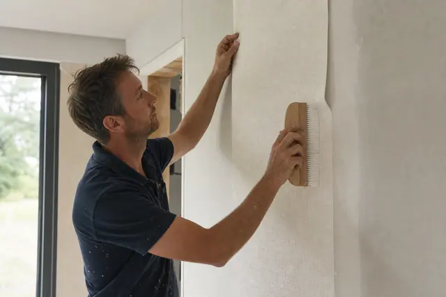 Pose d'un lé de papier peint intissé sur un mur avec brosse à maroufler