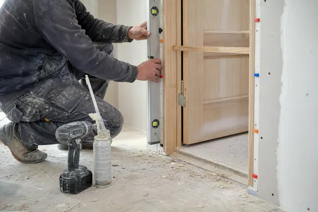 Menuisier réglant l’aplomb du bâti d’un bloc-porte intérieur au niveau à bulle