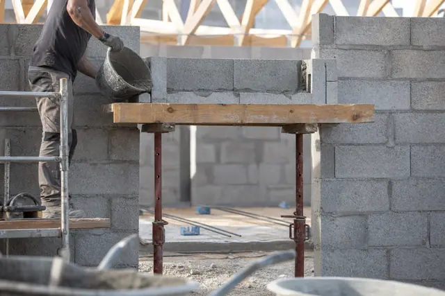 Maçon coulant du béton dans une file de blocs en U ferraillés au-dessus d’une porte