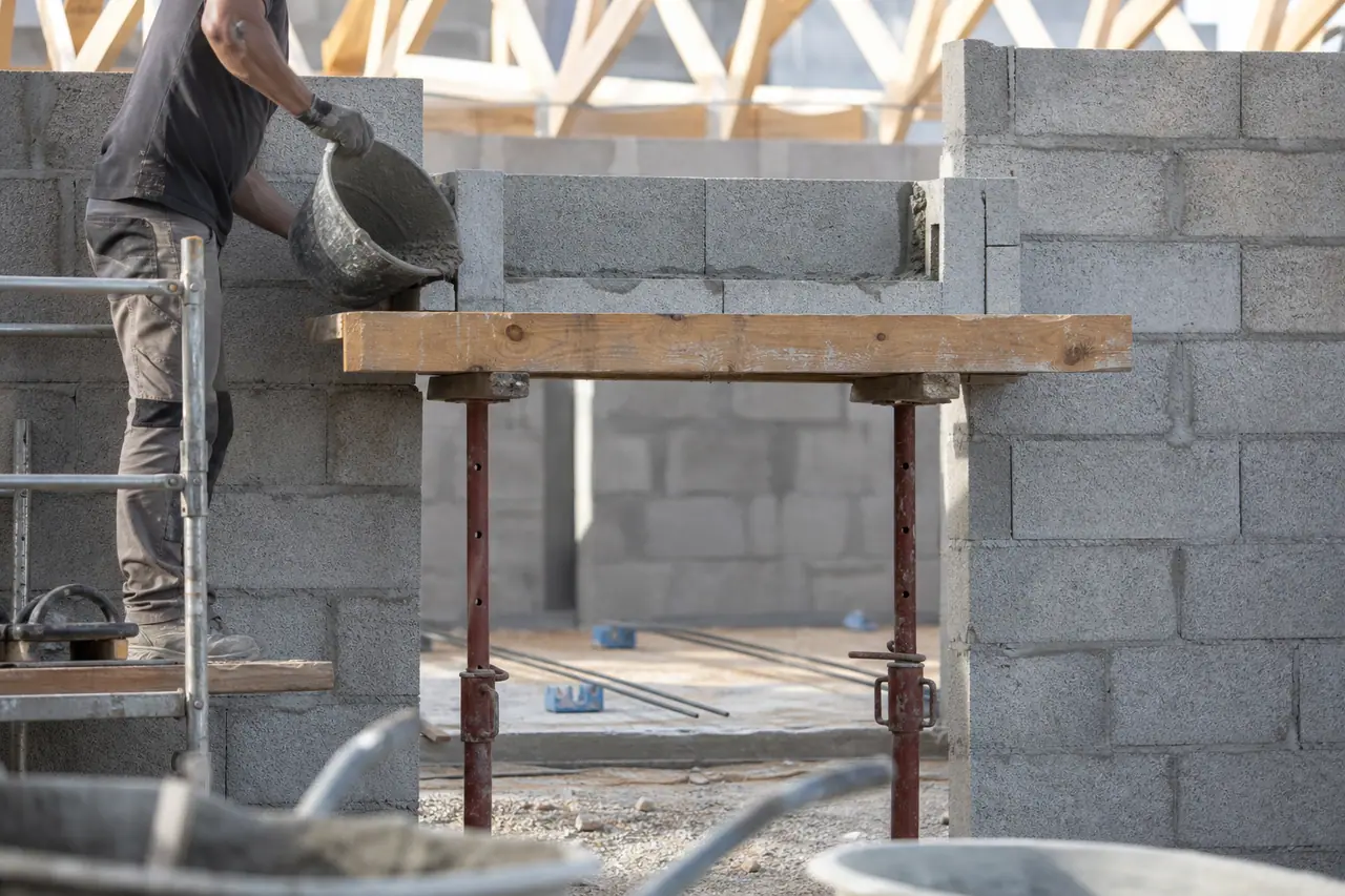 Maçon coulant du béton dans une file de blocs en U ferraillés au-dessus d’une porte