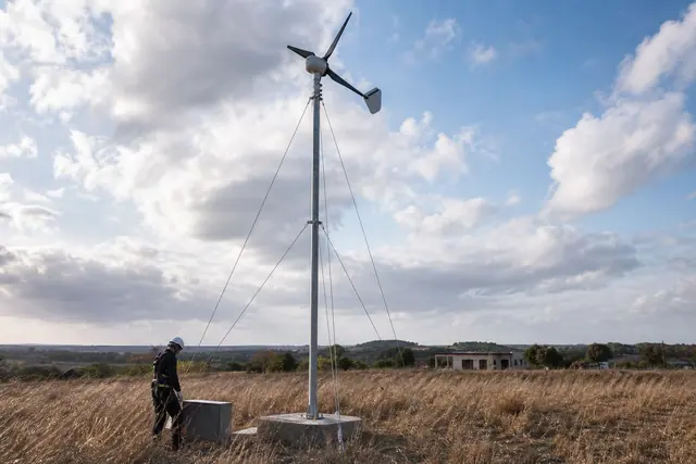Petite éolienne sur mât dans un terrain rural dégagé près d’une maison.