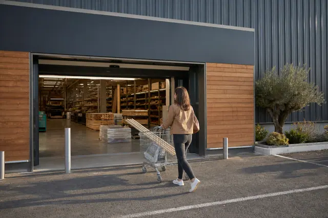 Cliente avec chariot devant un magasin de bricolage ouvert le dimanche.
