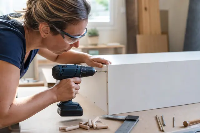 Bricoleuse vissant un caisson mélaminé avec une perceuse-visseuse compacte et embout Pozidriv.