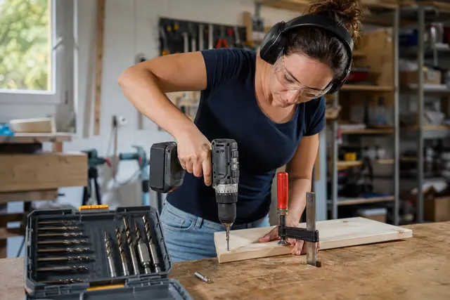 Bricoleuse équipée vissant une planche de bois avec une perceuse sans fil
