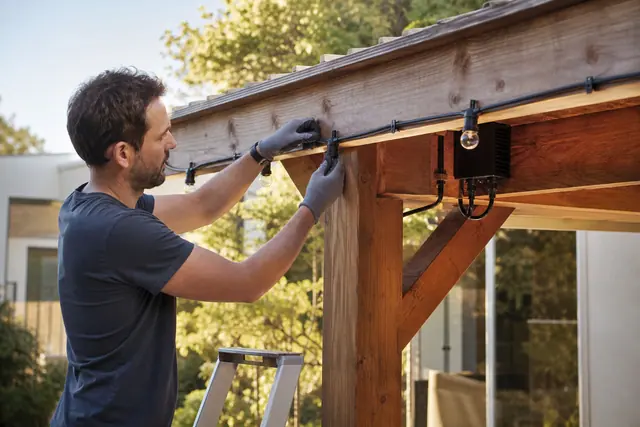 Installation sécurisée d’une guirlande extérieure sur une pergola avec raccords protégés.