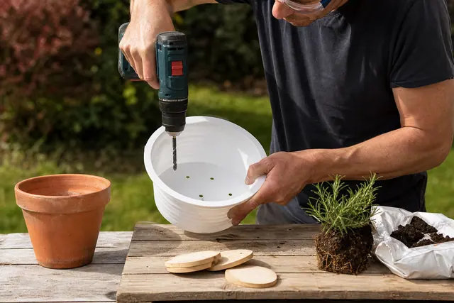 Seau recyclé percé et garni de plantes fleuries sur une terrasse