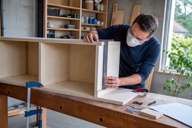Personne assemblant un caisson de bibliothèque en contreplaqué dans un atelier domestique.