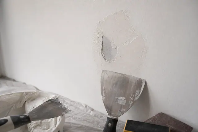 Trou dans une cloison en placo en cours de rebouchage avec spatule et enduit