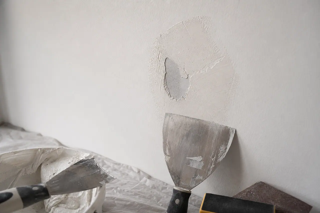 Trou dans une cloison en placo en cours de rebouchage avec spatule et enduit