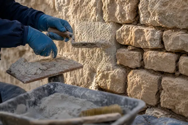 Mains gantées serrant du mortier de chaux au fer à joint dans un mur de moellons