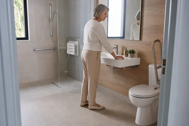 Salle de bains accessible avec douche sans seuil, barres d’appui et lavabo suspendu.