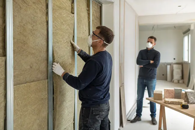 Artisan isolant un mur intérieur pendant qu’un propriétaire compare des matériaux.