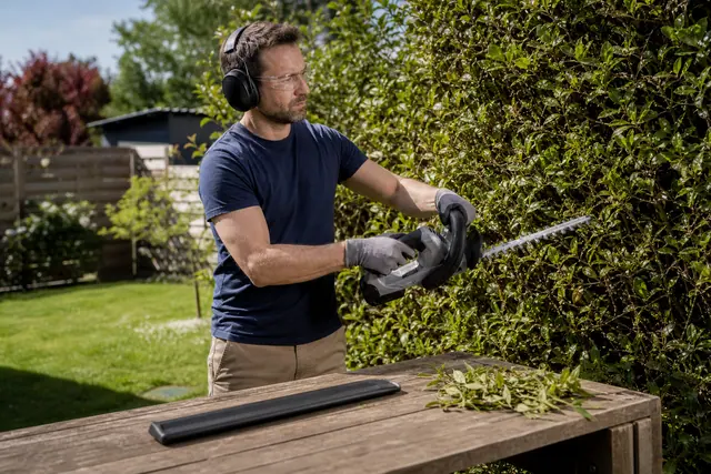 Jardinier équipé taillant une haie depuis le sol avec un taille-haie sans fil