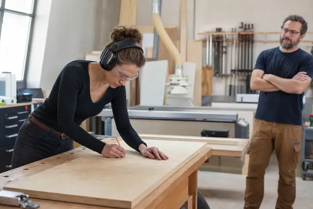 Débutante équipée préparant une planche dans un atelier bois partagé sécurisé.