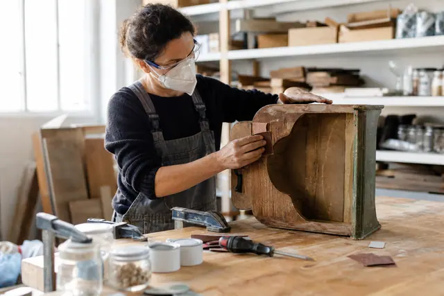 Personne rénovant un petit meuble en bois dans un atelier de réemploi.