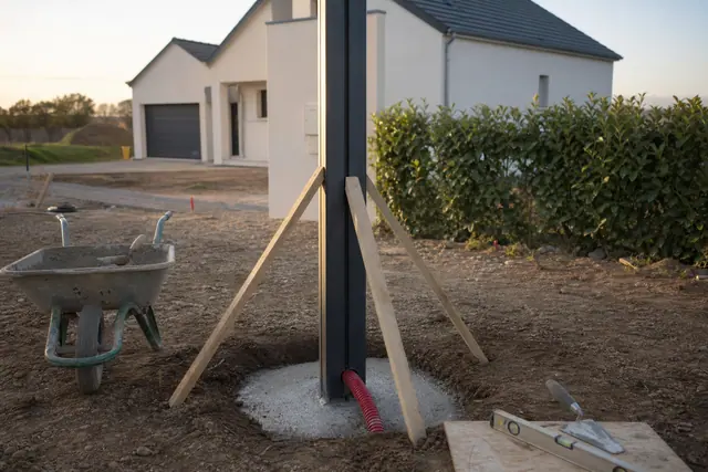 Poteau de portail en aluminium étayé au-dessus d’un massif de béton fraîchement coulé